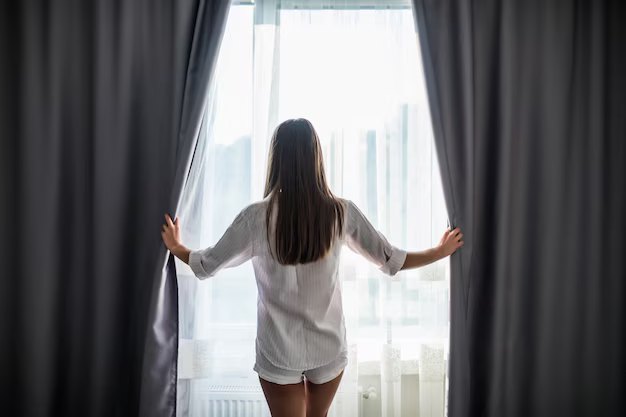 Person opening the curtains of a window to let natural light in