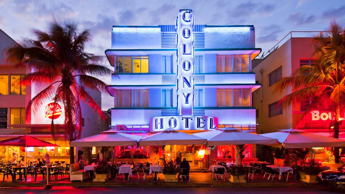 Fachada art déco del Colony Hotel en Ocean Drive, Miami Beach, con su letrero vertical de neón azul al anochecer
