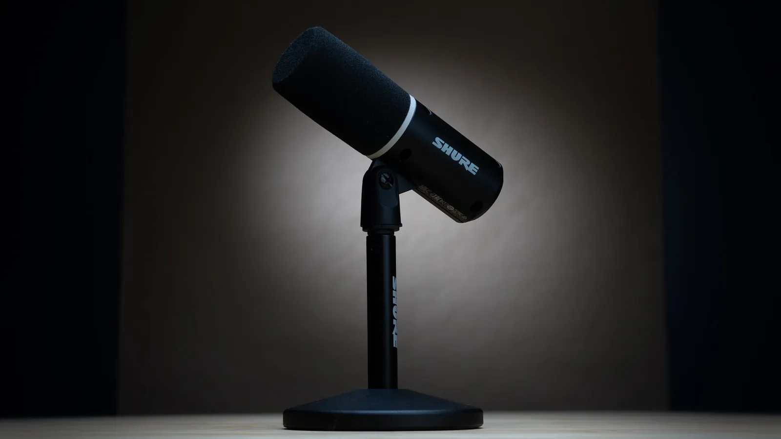 Black Shure MV6 Gen 2 microphone on its desktop stand, lit against a dark background